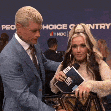 a man in a suit and tie is talking to a woman holding a microphone and a magazine that says live