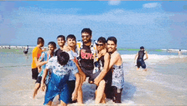 a group of young men are standing on a beach . one of the men is carrying another man on his shoulders .