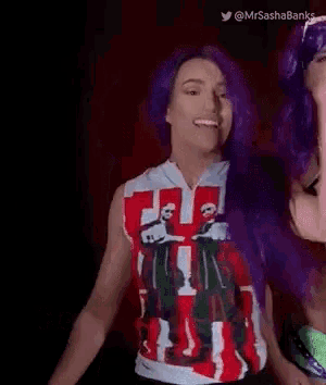 a woman with purple hair is smiling and wearing a red , white and black shirt .
