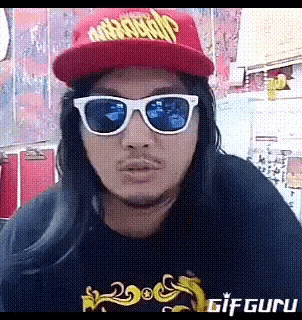 a man with long hair wearing sunglasses and a red hat with the word abercrombie on it