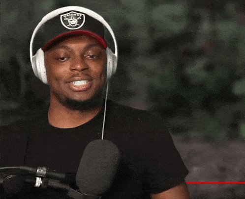 a man wearing headphones and a raiders hat is smiling