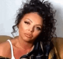 a woman with curly hair is sitting on a couch and looking at the camera .