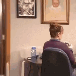 a woman in a purple sweater is sitting at a desk in front of a painting .