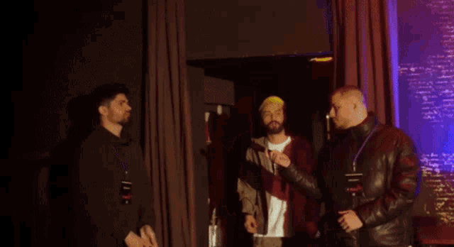 a man with a beard wearing a stussy shirt stands next to another man