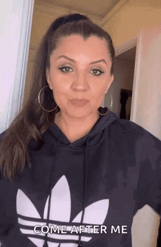 a woman wearing a black adidas hoodie is standing in front of a door
