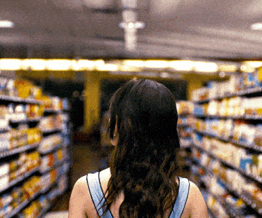 a woman in a blue tank top is walking through a grocery store aisle