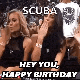 two women are sitting in the stands at a basketball game and one is blowing a kiss .