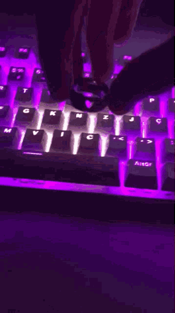 a person is typing on a keyboard that has purple lights on the keys