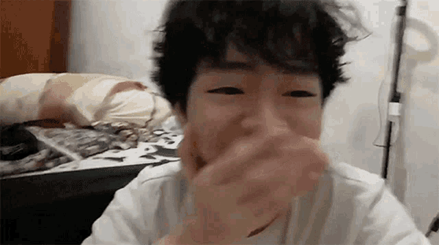 a young man with curly hair is covering his mouth with his hand .