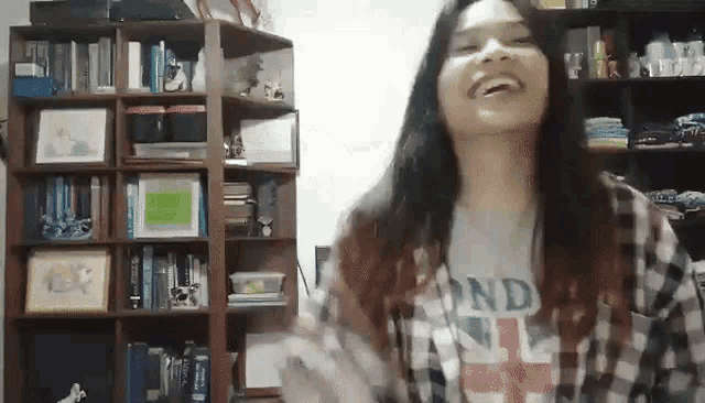 a girl wearing a london t-shirt is laughing in front of a bookshelf