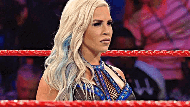 a woman with blonde hair and blue highlights is standing in a wrestling ring