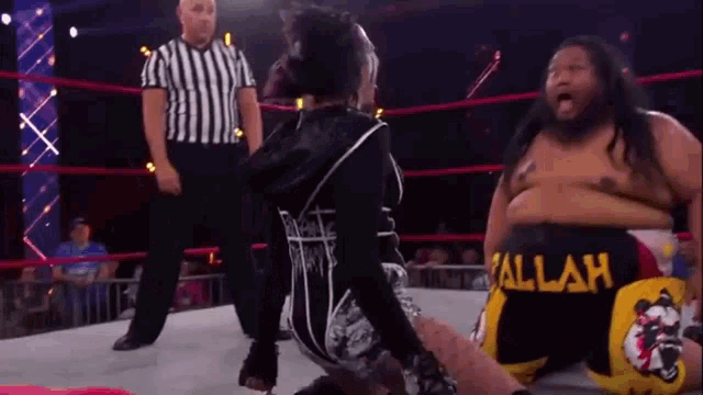 a woman is kneeling down in a wrestling ring while a referee looks on .