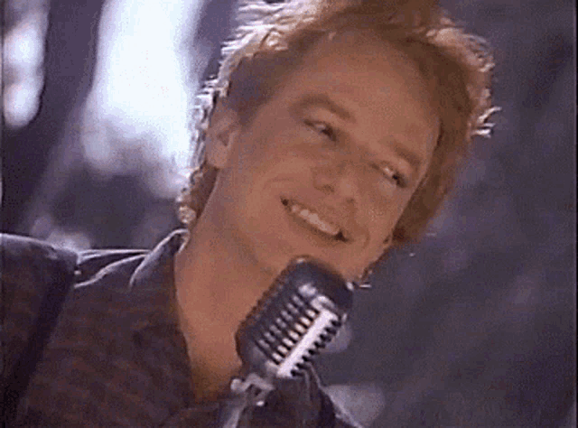 a man is singing into a microphone and smiling while looking at the camera .