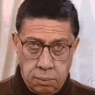 a man wearing glasses and a turtleneck is making a funny face .