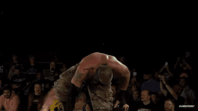 a group of wrestlers are fighting in a wrestling ring while a crowd watches .