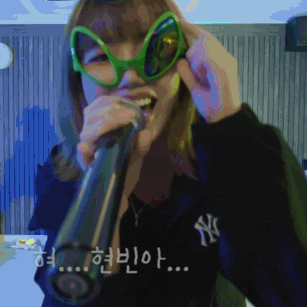 a woman singing into a microphone wearing green glasses and a ny jacket