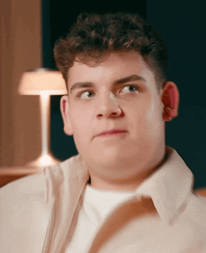a young man with curly hair looks at the camera in front of a lamp