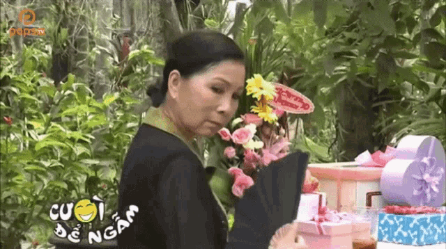a woman is standing in front of a bunch of flowers and boxes with cuoi de ngam written on it