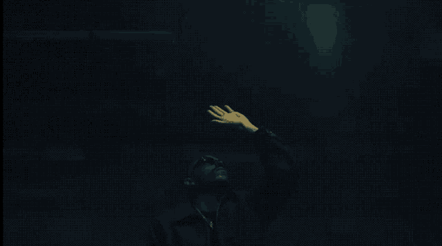 a person in a dark room reaching up to a light