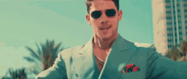 a man in a suit and sunglasses is holding a spray bottle and smiling .