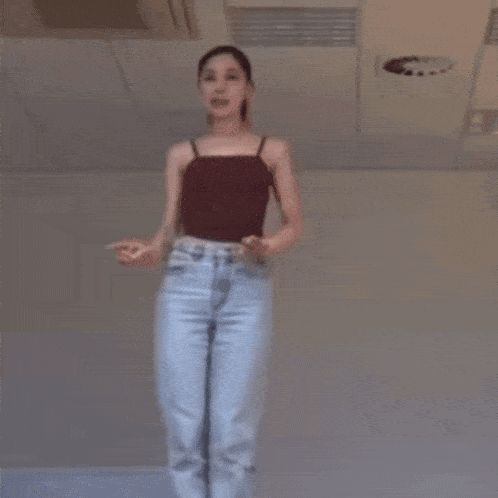 a woman in a red tank top and blue jeans is dancing in a room .