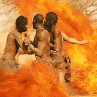 three naked men are standing in front of a large fire