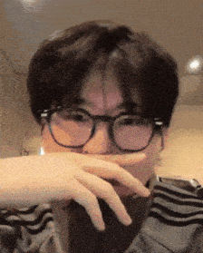a man wearing glasses is covering his mouth with his hands