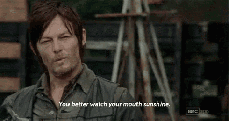 a man is standing in front of a wooden structure and saying `` you better watch your mouth sunshine . ''
