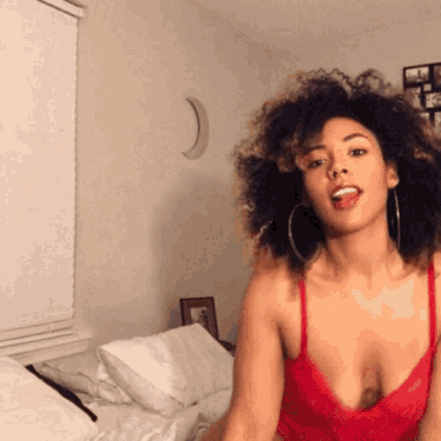 a woman with curly hair is wearing a red bra and hoop earrings
