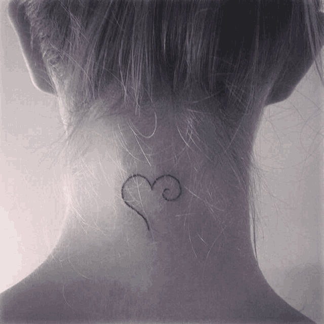 a woman has a small tattoo of a heart on the back of her neck