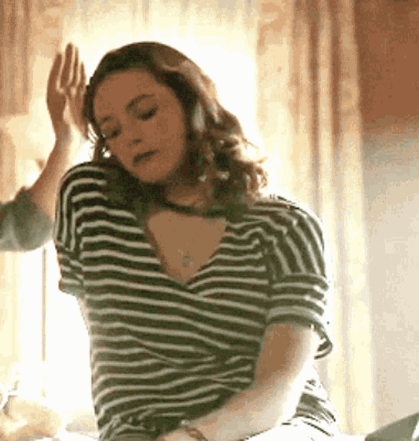 a woman in a striped shirt is sitting on a bed with her hand on her head