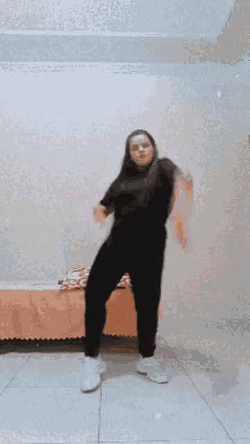 a woman in a black shirt and white shoes is dancing in a room