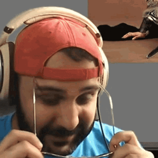 a man wearing headphones and a red hat is adjusting his glasses .