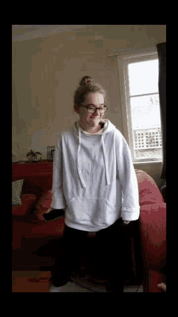 a girl wearing glasses and a white hoodie stands in a living room