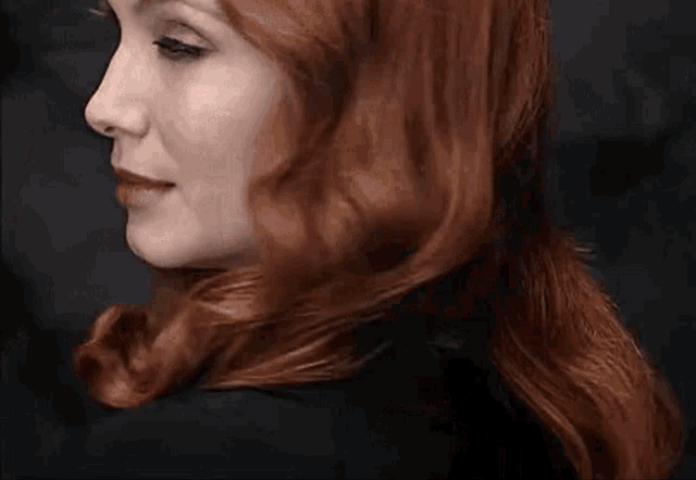 a woman with red hair and blue eyes looks at the camera