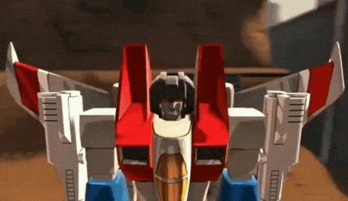 a robot with red white and blue wings is standing on a sandy surface