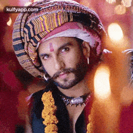 a man with a beard wearing a turban and a necklace is looking at the camera .