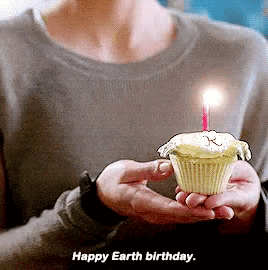 a woman is holding a cupcake with a lit candle and the words happy earth birthday