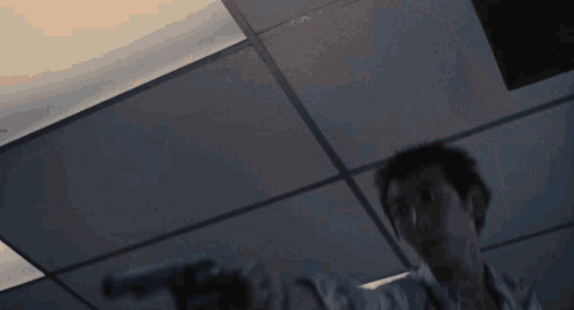 a man in a floral shirt is pointing a gun at the ceiling
