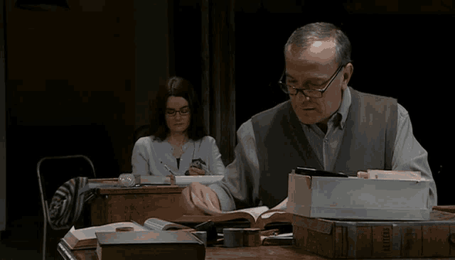 a man sits at a desk with a stack of books and a box that says ' military ' on the side