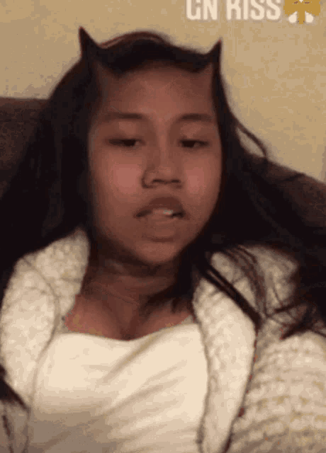 a girl with horns on her head is laying on a couch with a gn kiss emoji behind her