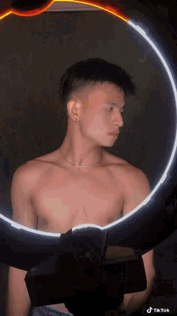 a shirtless man is looking at himself in a mirror with a tiktok logo on the bottom right