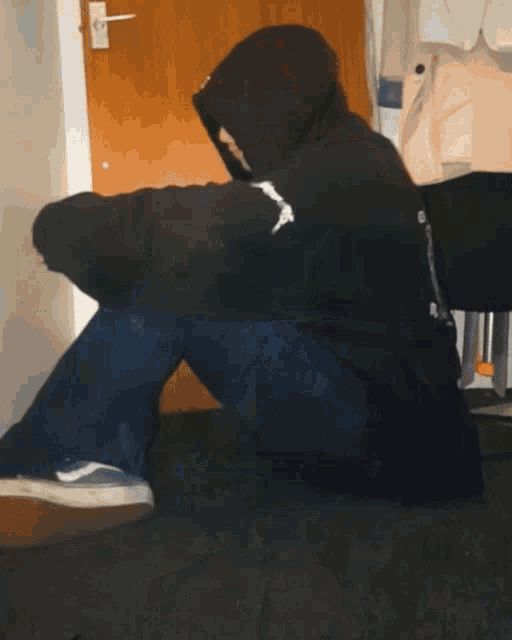 a person wearing a black hoodie with the word jesus on it sits on the floor