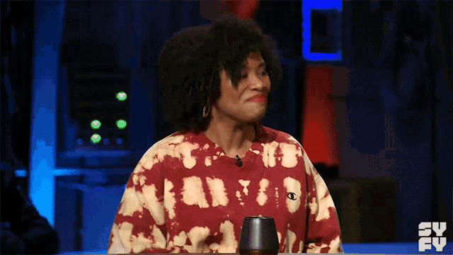 a woman wearing a tie dye sweatshirt is sitting at a table