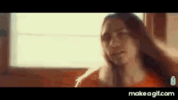 a woman with long hair is sitting in front of a window and looking at the camera .