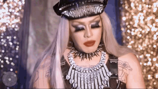 a drag queen wearing a hat and a necklace with spikes .