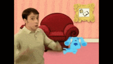 a man is standing next to a blue dog in a living room with a red chair .