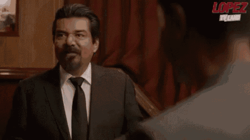 a man in a suit and tie is talking to another man in a room .