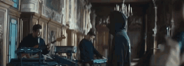 a man in a hoodie is standing in a room with a band playing instruments .