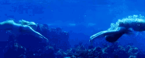 two mermaids are swimming in the ocean holding hands